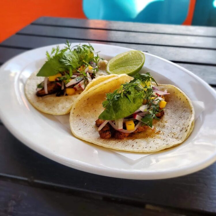 2 shrimp tacos on a white plate topped with onions and avocado