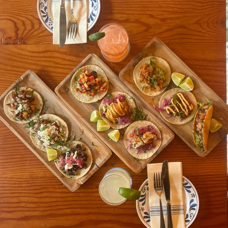 3 rectangular wooden plates with 3 tacos on each plate on a wooden table