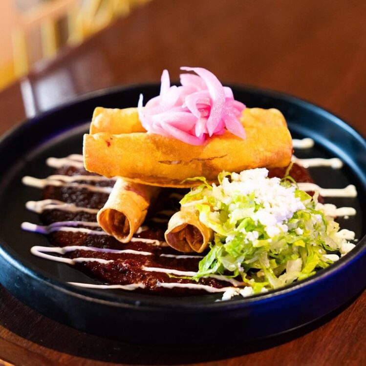 Flautas on mole sauce on black plate