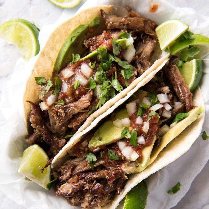 2 barbacoa tacos topped with cilantro, onion and avocado