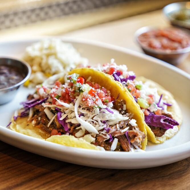 Plate of 2 carnitas tacos with beans and rice