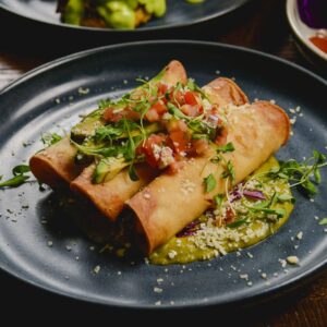 Black Plate of Taquitos surrounded by other plates of food