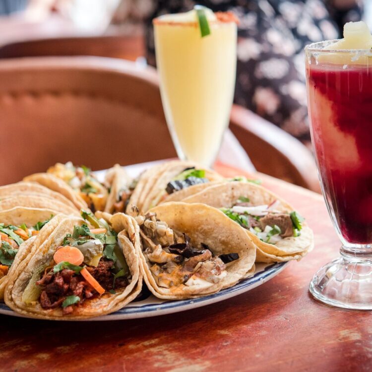 Plate with variety of tacos and 2 frozen margaritas on wooden table