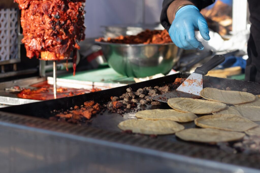 StreetVendorGrillingTortillasAndChoppedAlPastorMeatOn