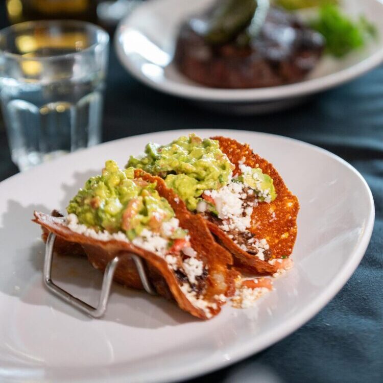tacos with a shell made out of grilled cheese, filled with chopped ribeye steak, pico de gallo, and topped with fresh guacamole and crumbled queso fresco.