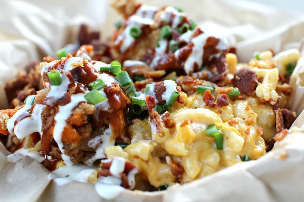 Loaded nachos with crispy bacon, melted cheese, green onions, and white crema drizzled on top in a parchment-lined bowl area.