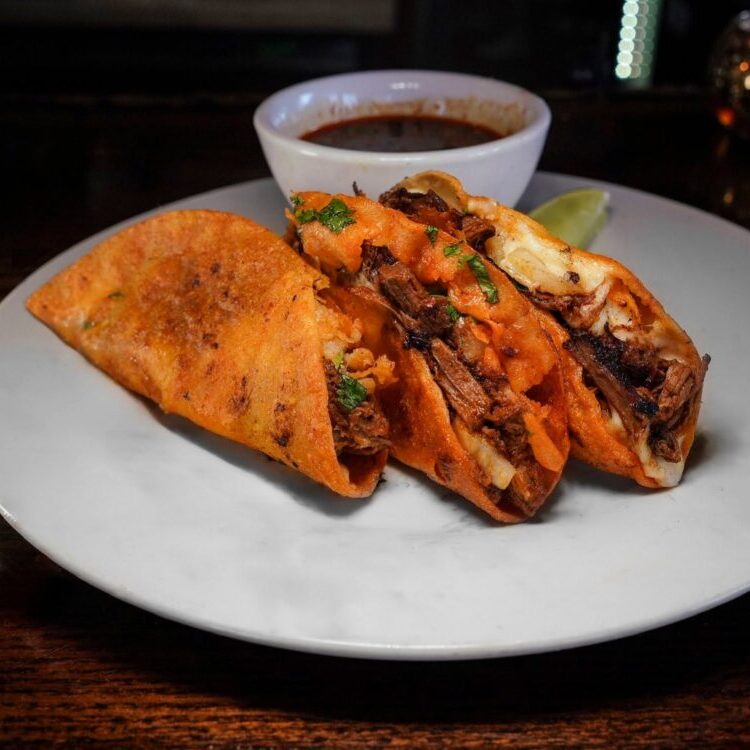 Two tacos filled with shredded beef and cilantro on a white plate, with a side of salsa and lime in the background.