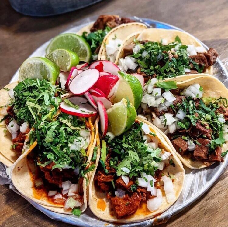 Plate of soft beef tacos topped with onions and cilantro, with lime wedges and radish slices on the side, on a metal platter