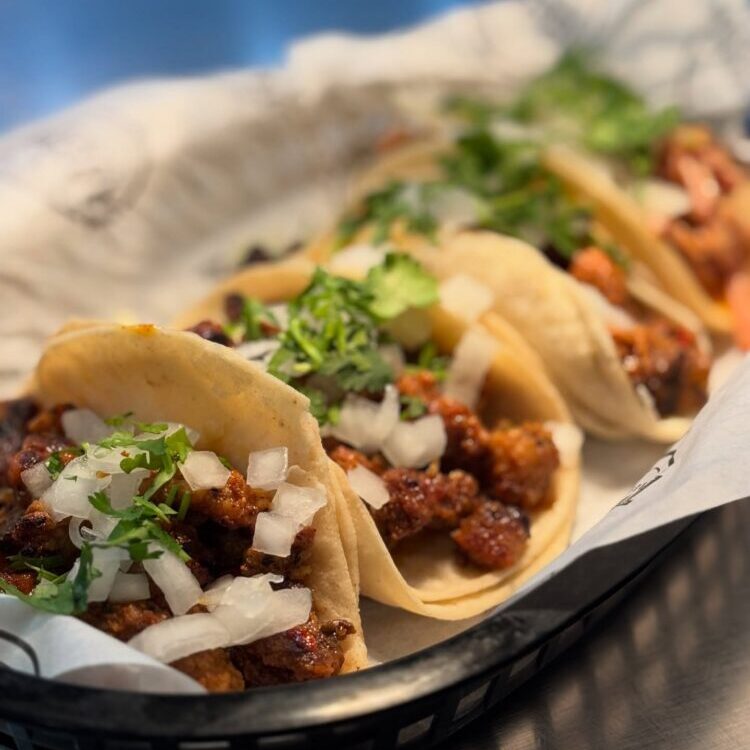 Tacos filled with seasoned ground meat, onions, and cilantro in a basket-lined tray.