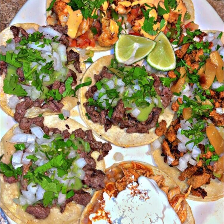Taco plate with beef and shrimp toppings, onions, cilantro, lime wedges, and various salsas; 'Happy Cinco de Mayo' caption above.