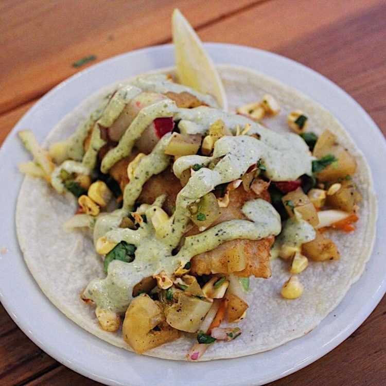 Tortilla with roasted potatoes, corn, cilantro, and creamy verde sauce, garnished with a lime wedge on a white plate.